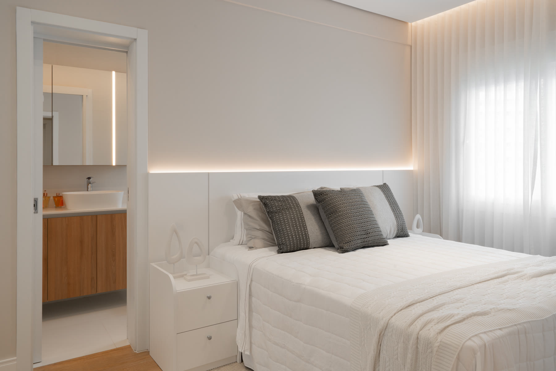 Quarto com cabeceira branca e acesso ao banheiro